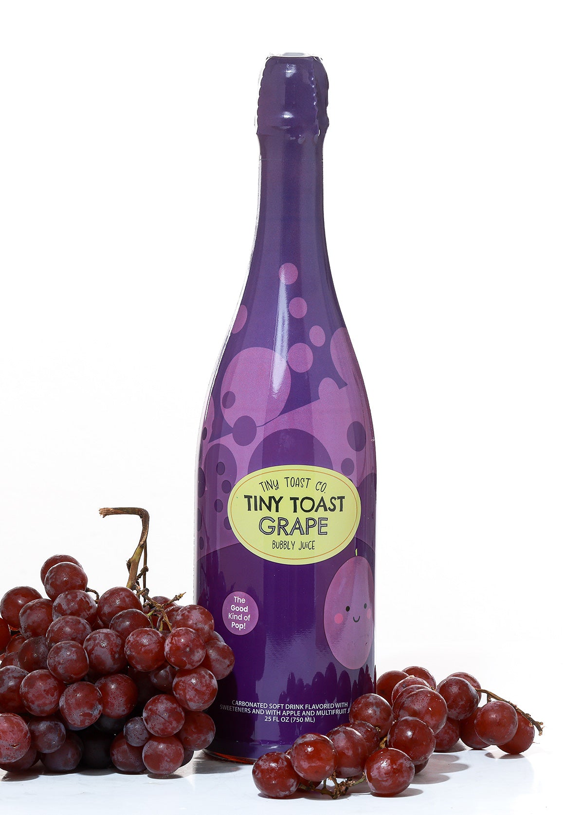 A bottle of Tiny Toast Co. Tiny Toast Grape Bubbly Juice surrounded by red grapes on a white background.